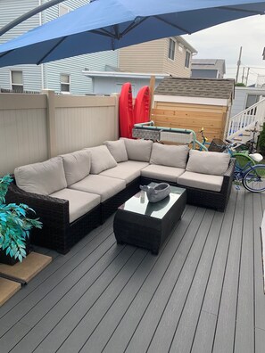 Relax on the patio with a comfortable sofa and table, shaded by a large umbrella.