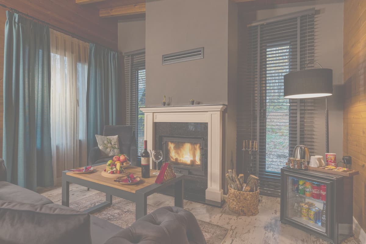 A cozy living room with a fireplace, a coffee table with fruits and a bottle, and a refrigerator with beverages.