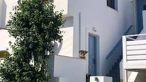 Ein weißes Gebäude mit blauer Tür und Fenstern, einer Treppe und einem Baum davor.