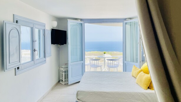 Ein Schlafzimmer mit Bett, Fernseher und einem offenen Balkon mit Meerblick.