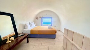 Ein Schlafzimmer mit Bett, Nachttisch mit Fernbedienung, Fenster mit Meerblick und einer Holzbank an der Wand.