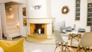Ein gemütliches Wohnzimmer mit Kamin, einem für zwei Personen gedecktem Esstisch und einer Treppe, die zu einer oberen Ebene führt.