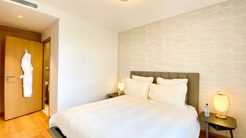 A hotel room with a large bed, a nightstand with a lamp, a robe hanging on the door, and a textured wall.