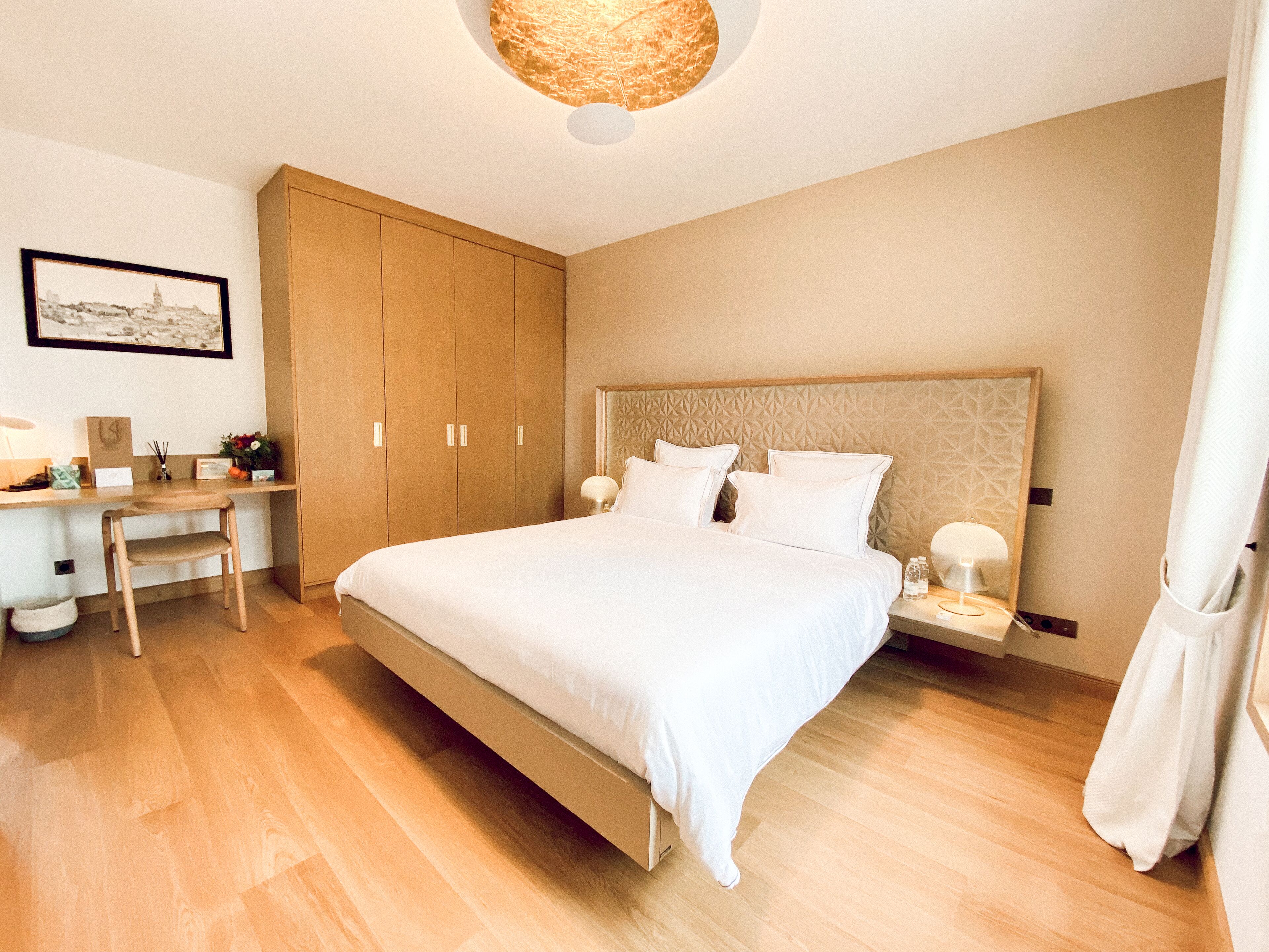 Un dormitorio con una cama grande, armario de madera, escritorio, silla y un cuadro enmarcado en la pared.