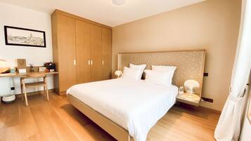 Un dormitorio con una cama grande, armario de madera, escritorio, silla y un cuadro enmarcado en la pared.