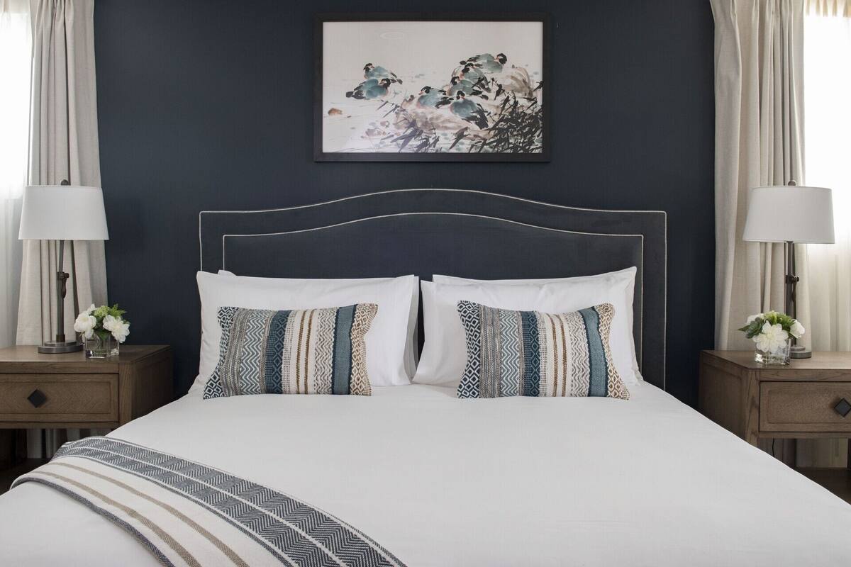 A neatly made bed with patterned pillows, a dark headboard, and a framed artwork above it.