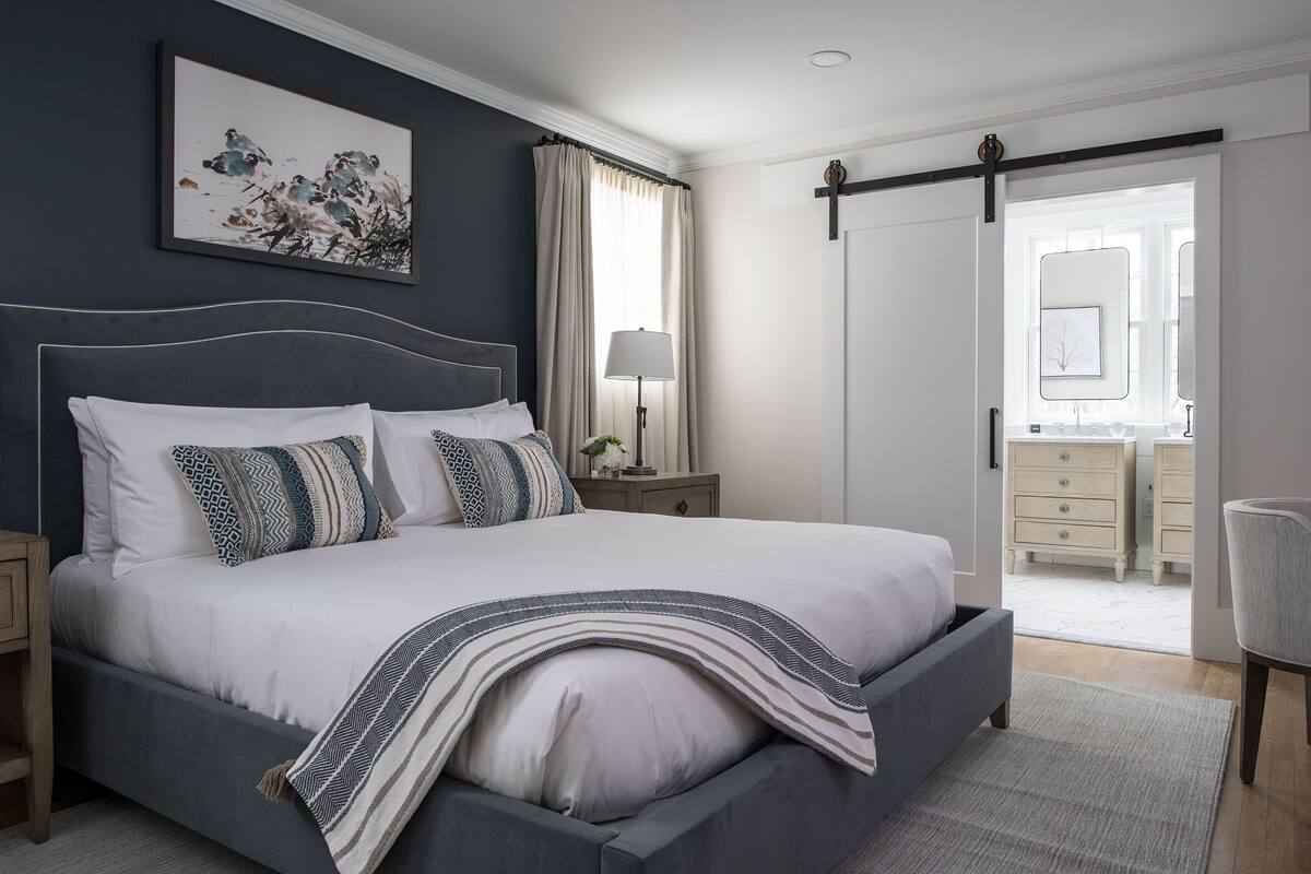 A bedroom with a bed, bedside tables, a lamp, a mirror, and a door leading to another room.