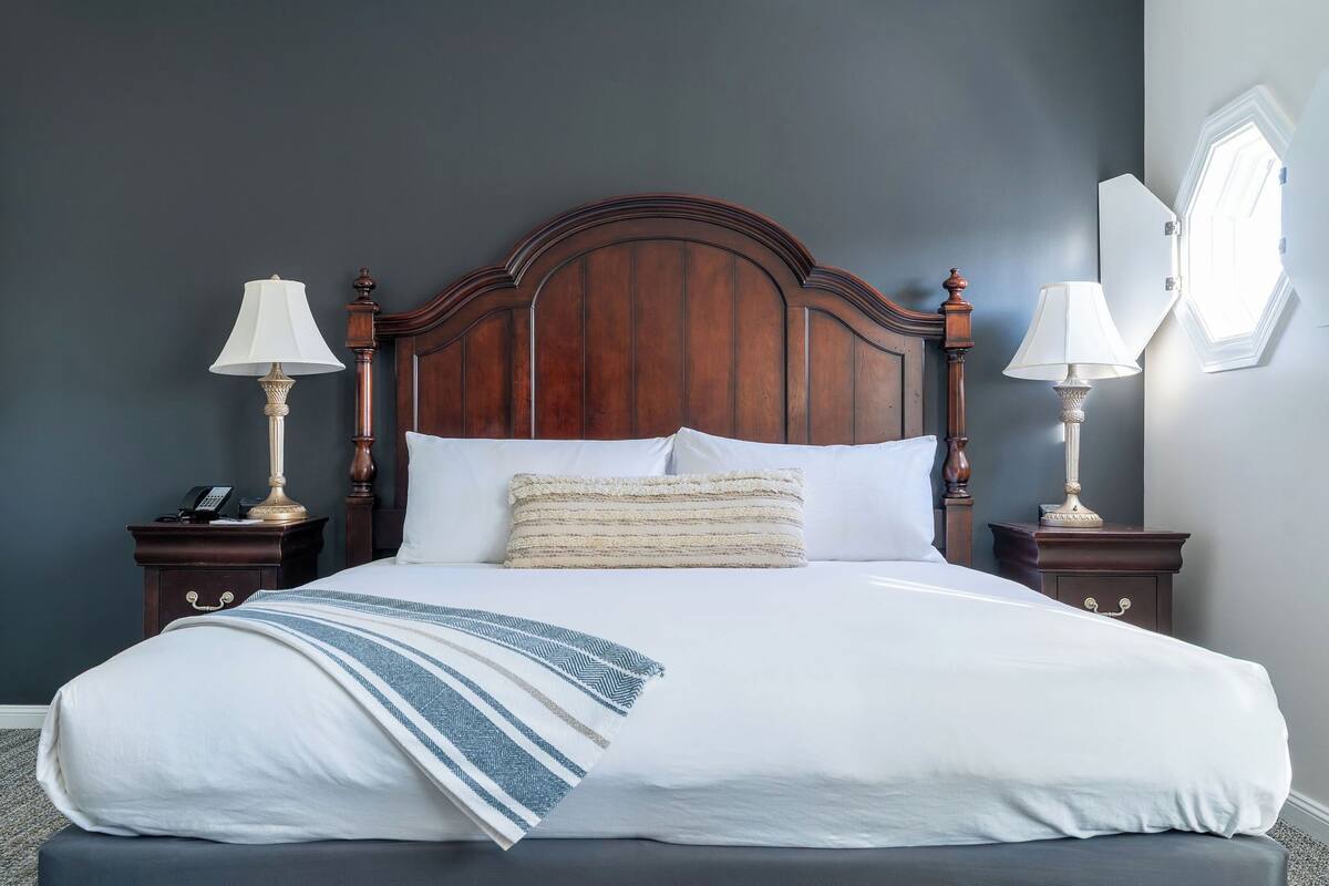 A neatly made bed with a wooden headboard, two bedside tables with lamps, and a wall-mounted light fixture.