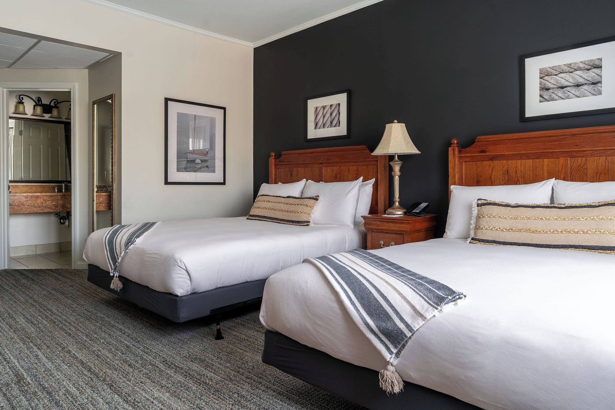 A hotel room with two beds, a wooden headboard, a nightstand with a lamp, and framed artwork on the wall.