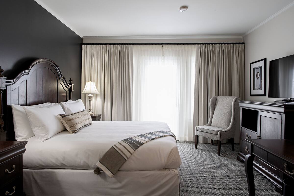 A hotel room with a large bed, a chair, a desk, and a television.