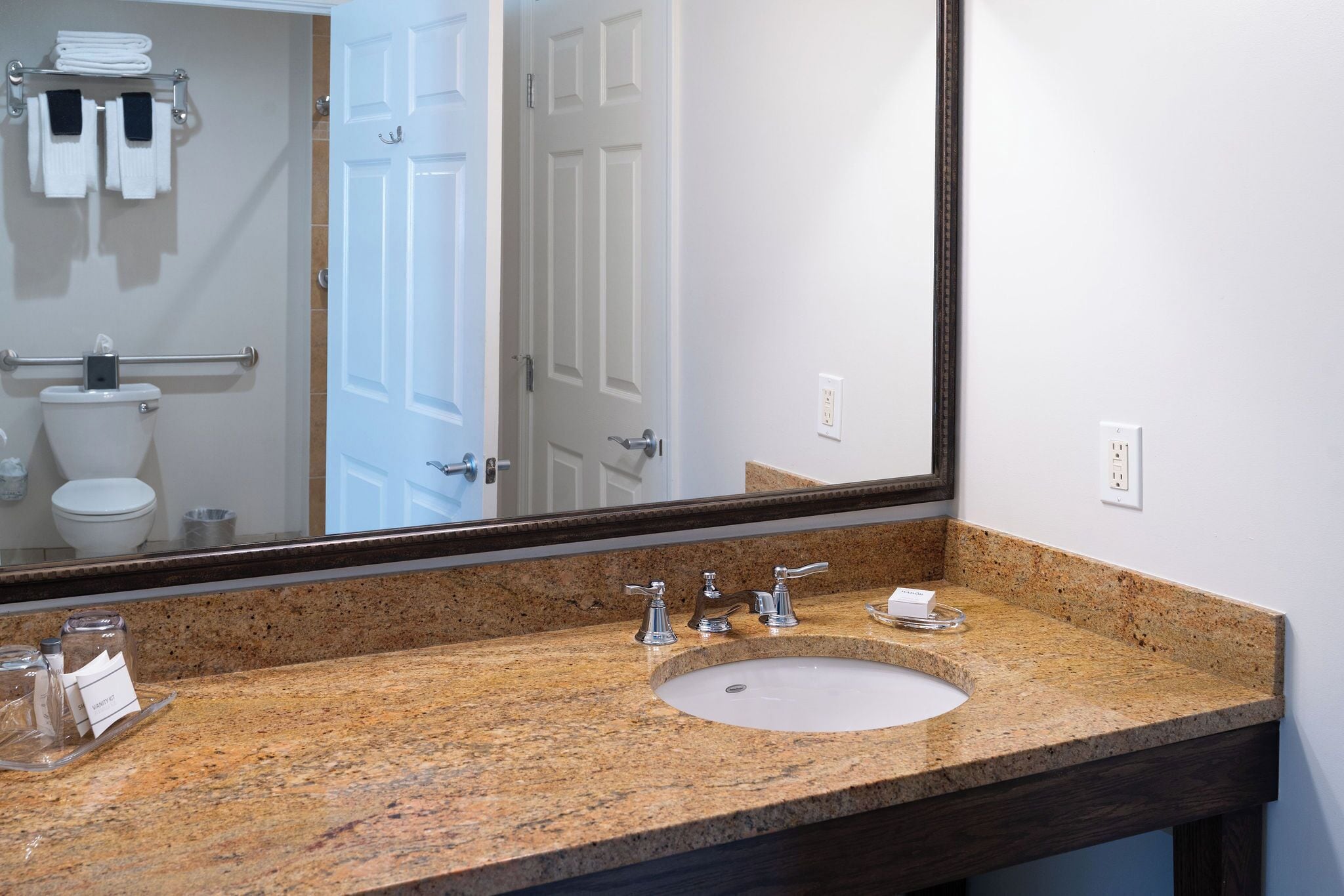 A bathroom with a granite countertop, a sink, and a large mirror.