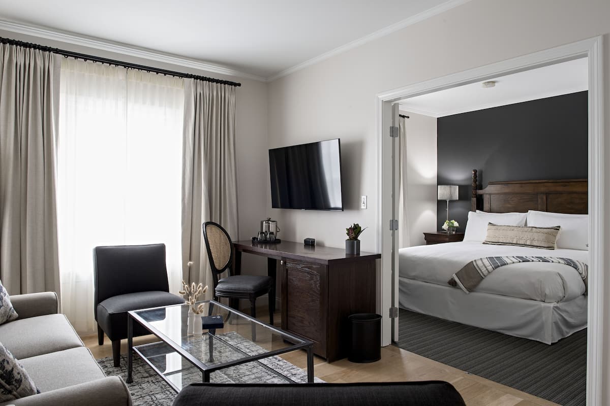 A modern hotel room with a bed, a desk, a chair, a TV, and a sofa.
