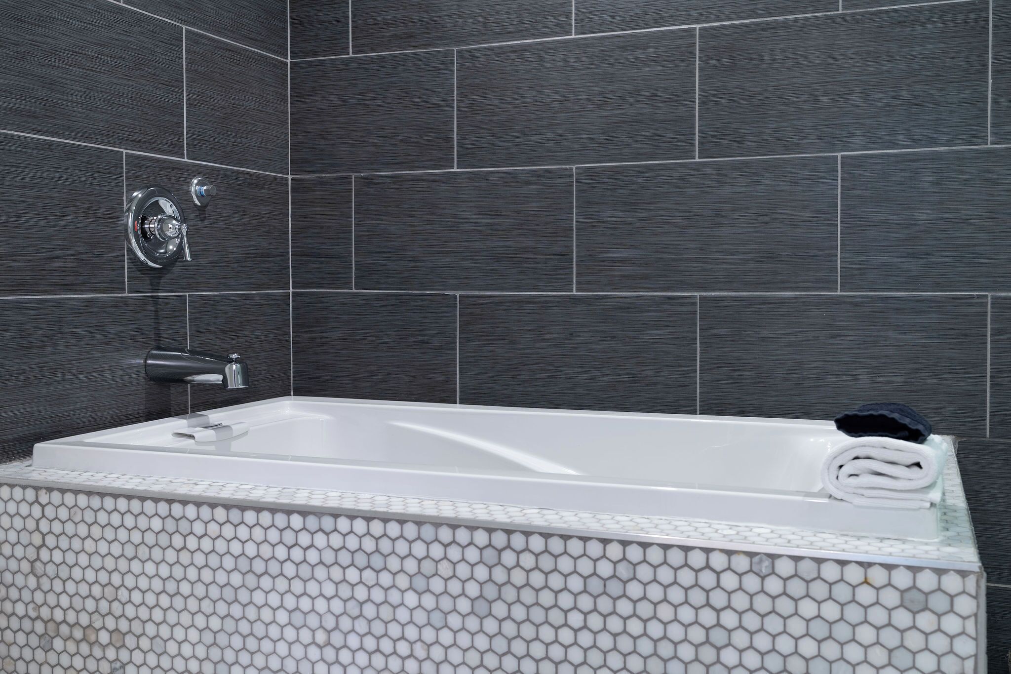 Un baño moderno con una bañera rectangular, un cabezal de ducha manual y una toalla en el borde.
