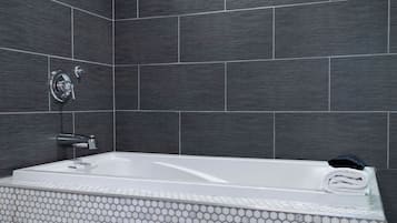 Un baño moderno con una bañera rectangular, un cabezal de ducha manual y una toalla en el borde.