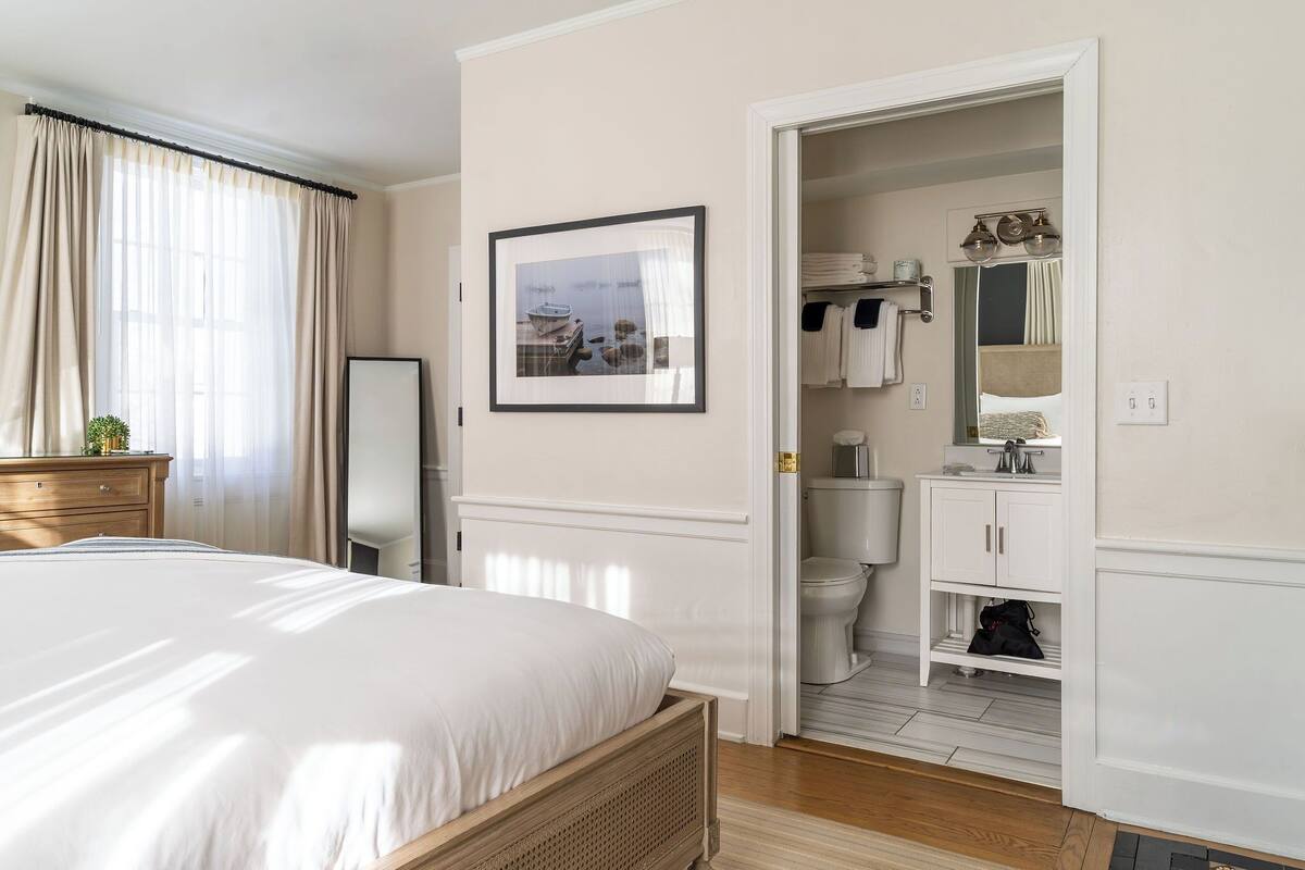 A bedroom with a bed, a bedside table, a wardrobe, and a bathroom visible through an open door.