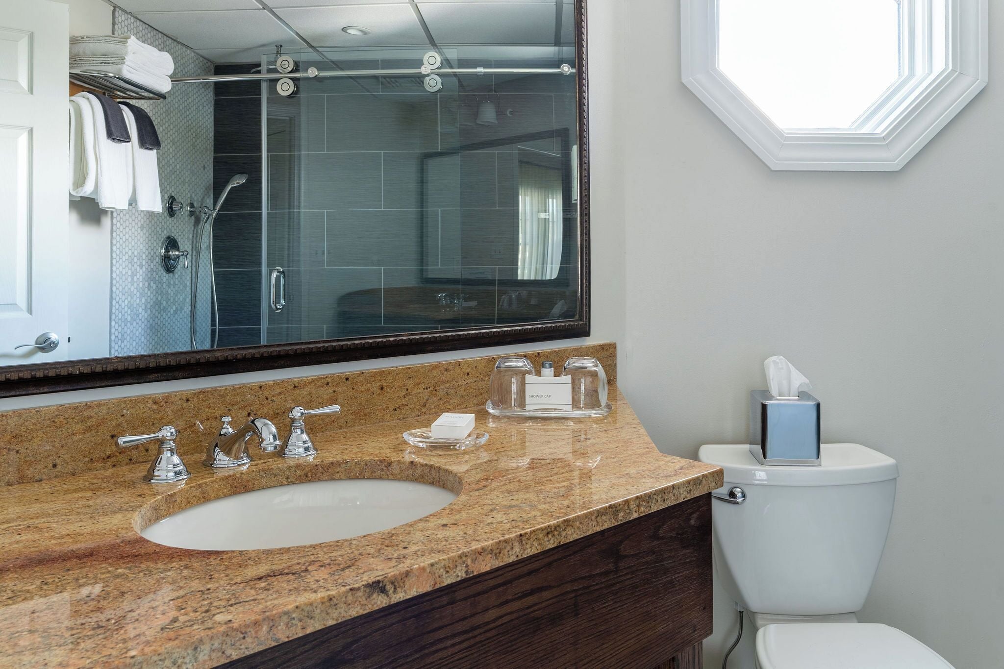 A bathroom with a granite countertop, a large mirror, a shower, and a toilet.