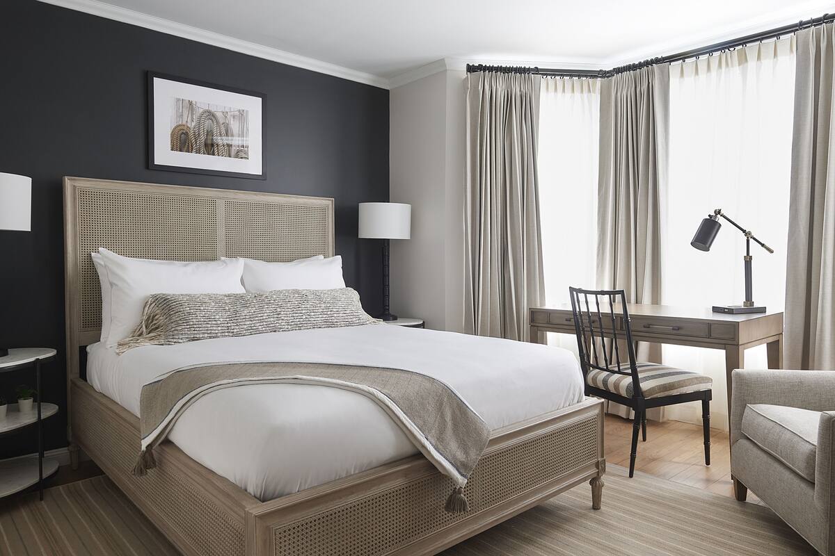 A neatly arranged hotel room with a large bed, a desk, and a chair.