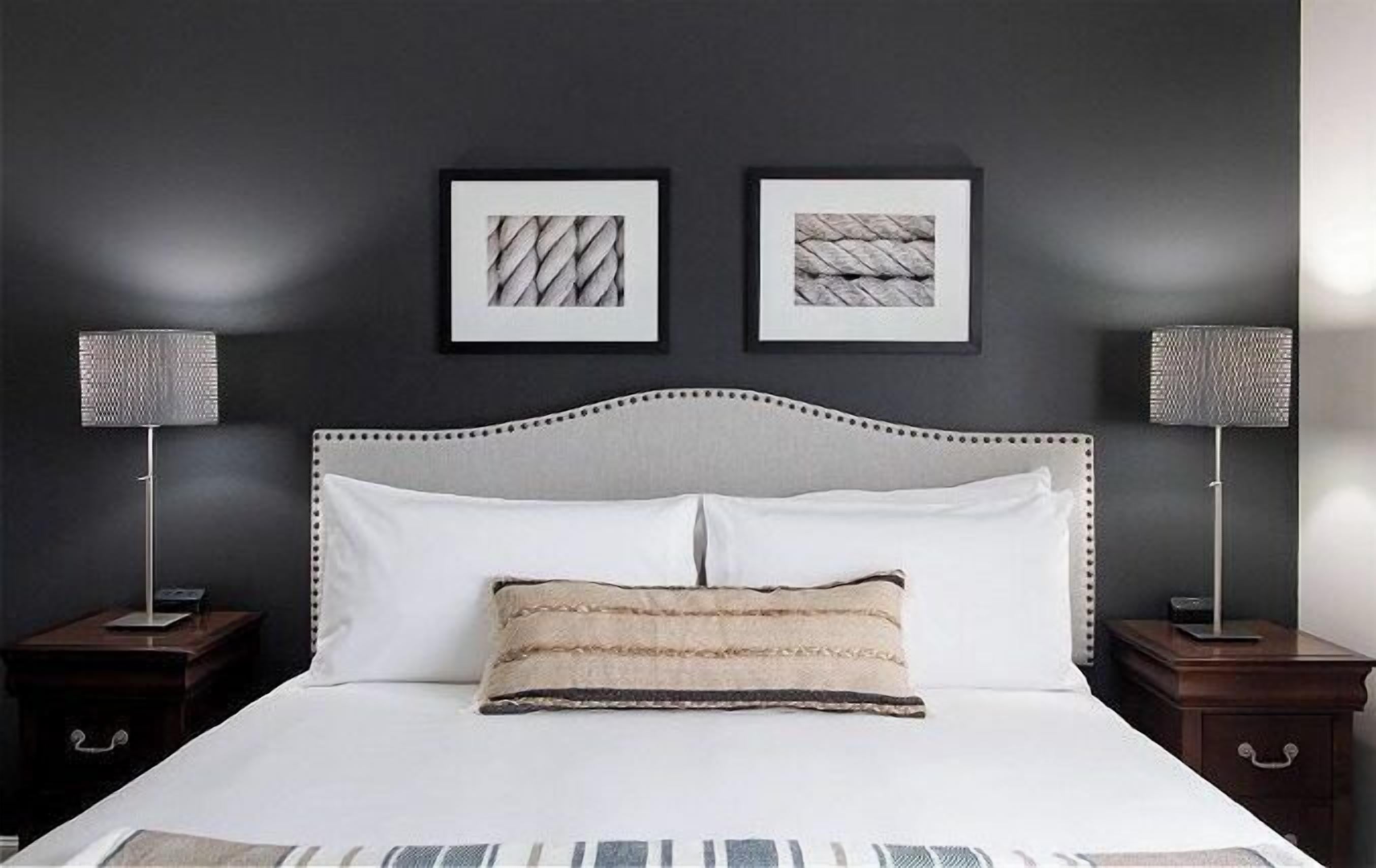 A neatly made bed with a white headboard and two pillows, flanked by two bedside tables with lamps.