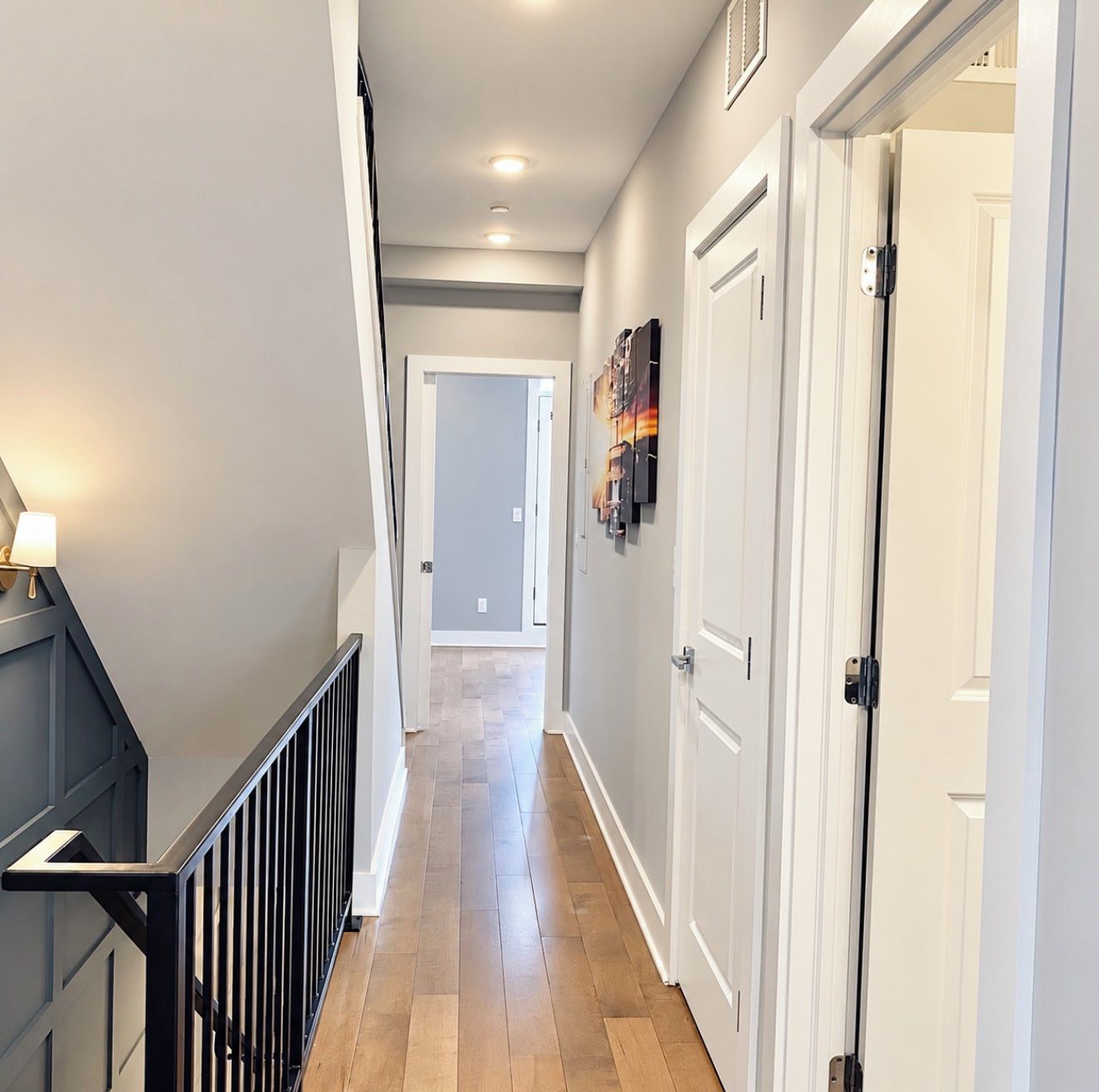 A hallway with a wooden floor, white walls, and a black railing.