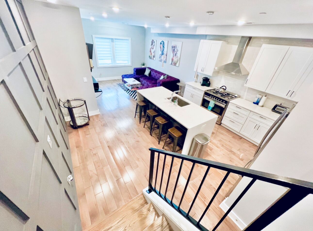 A modern kitchen with white cabinets, a central island with stools, and a dining area with a purple sofa.