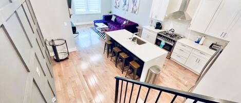 A modern kitchen with white cabinets, a central island with stools, and a dining area with a purple sofa.