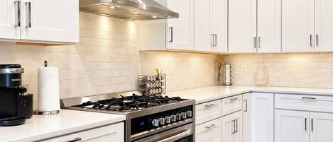 A modern kitchen with white cabinetry, stainless steel appliances, and a wooden floor.
