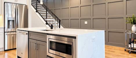 A modern kitchen with stainless steel appliances, a central island, and a staircase leading to an upper level.