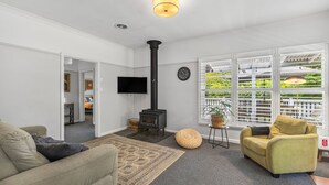 Una sala de estar con sofá, un sillón amarillo, un ventanal con persianas, chimenea y televisor de pantalla plana.
