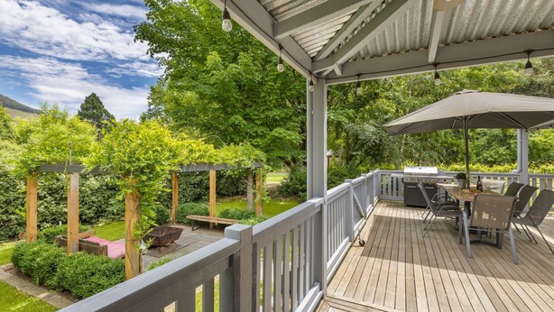 Una terraza techada al aire libre con una parrilla, asientos y una pérgola cubierta de plantas trepadoras.
