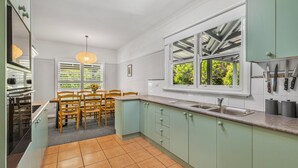 Una cocina moderna con armarios verde claro, un ventanal con vistas a la vegetación, un comedor con sillas de madera y un colgador para cuchillos.