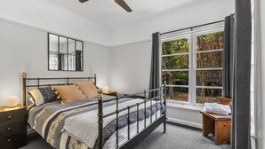 Un dormitorio con cama, mesitas de noche, un espejo y una ventana con cortinas.