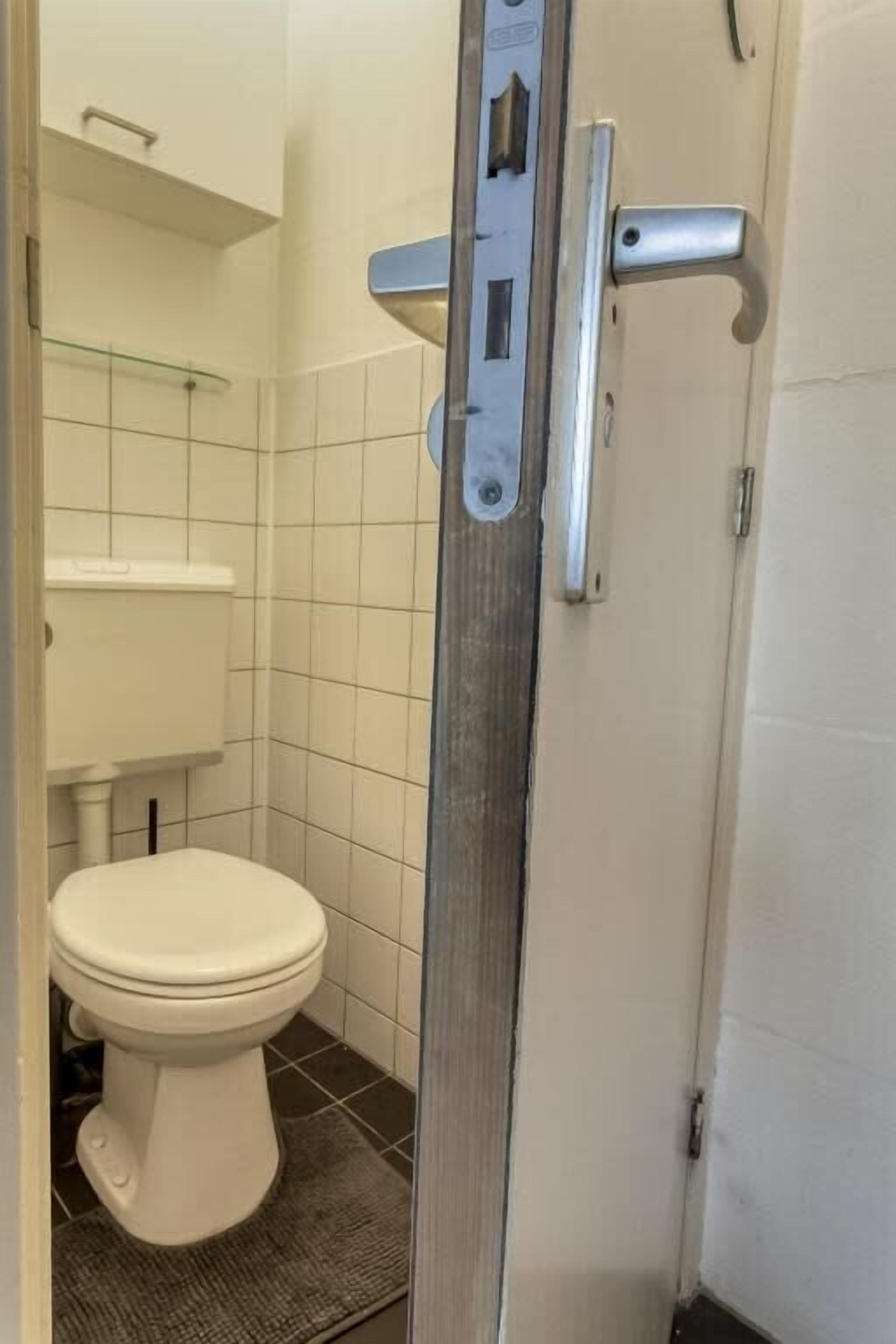 Un bagno con un WC bianco, cabina doccia in vetro e pavimento piastrellato.