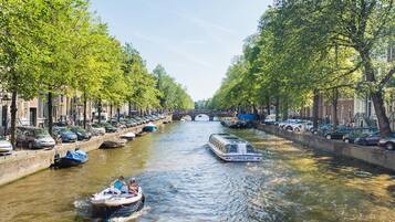 Een gracht met boten, omzoomd door bomen en parkeerauto's aan beide zijden.