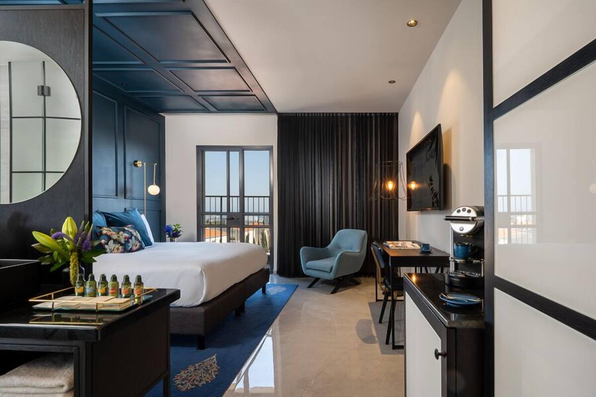 Una habitación de hotel moderna con una cama grande, un escritorio con silla, un televisor y un área de comedor con mesa y sillas.