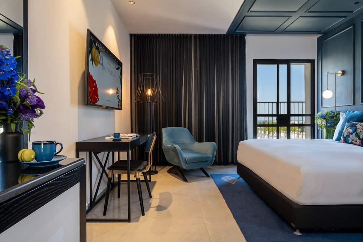 Habitación de hotel moderna con una cama, un escritorio, una silla, un ventanal grande y una cortina.
