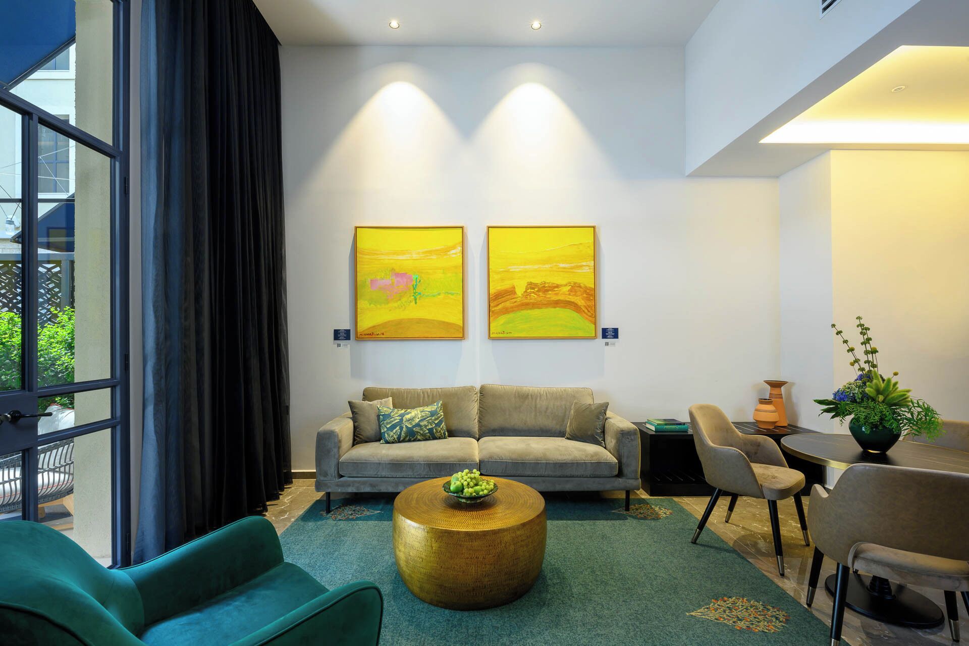 Una sala de estar moderna con un sofá gris, sillones turquesa, una mesa redonda de centro con un frutero y dos cuadros abstractos en la pared.