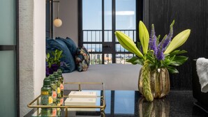 A modern room with a glass table displaying bottles and boxes, a potted plant with purple flowers, and a view of the outdoors through a large window. - Hotel Botanica- Limited Edition By Fattal (Haifa)