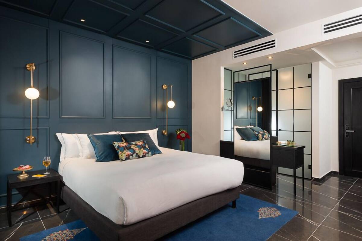 Un dormitorio moderno con una cama grande, paredes azul oscuro y un espejo de marco negro.