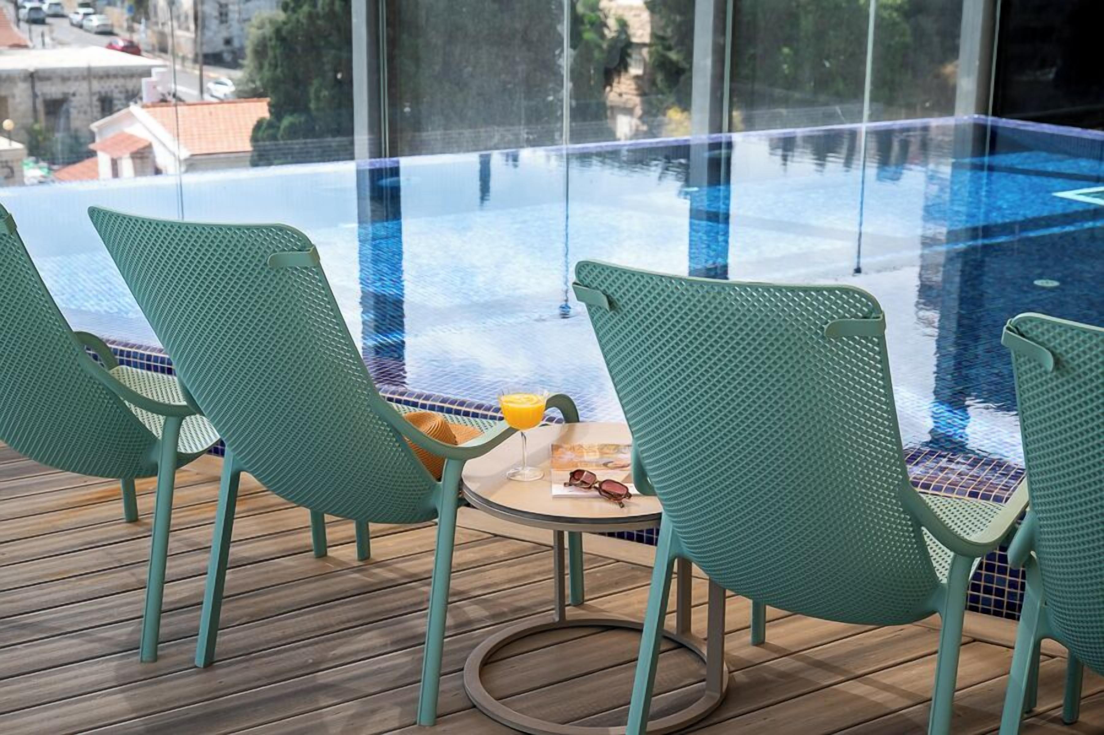 A glass-enclosed pool area with green chairs and a small table with a drink.