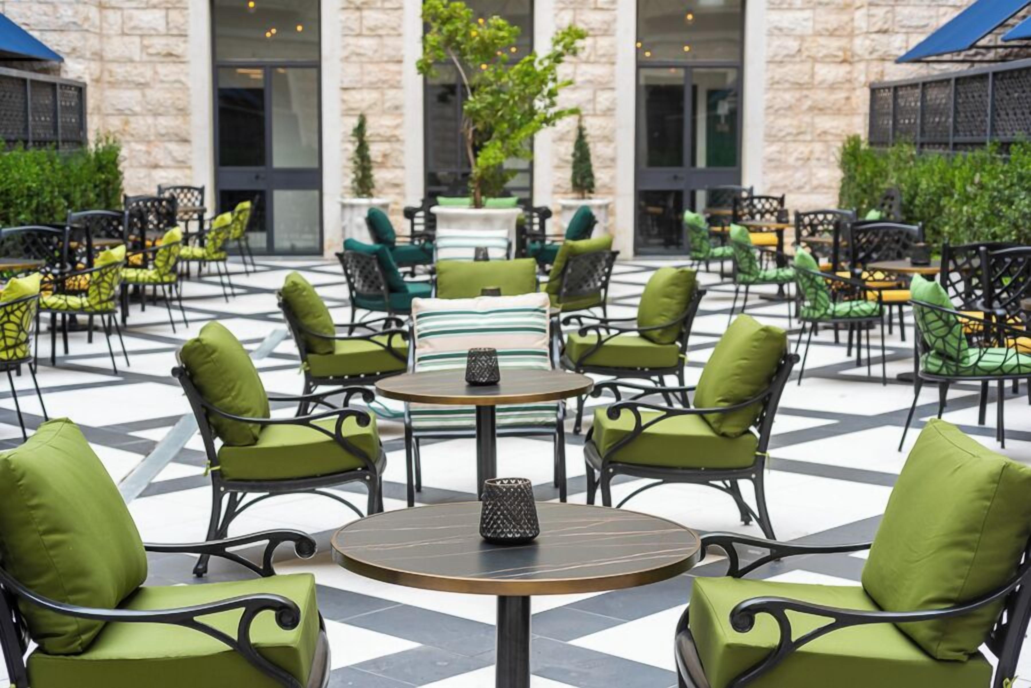 An outdoor patio with round tables and chairs, a stone building in the background, and a tiled floor.