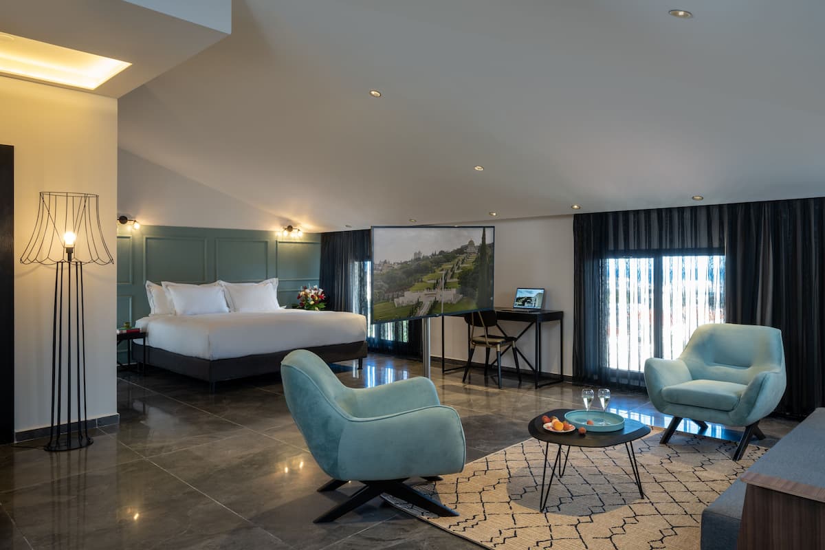 Una habitación de hotel moderna con una cama grande, dos sillones, un escritorio con una computadora portátil y un cuadro en la pared.