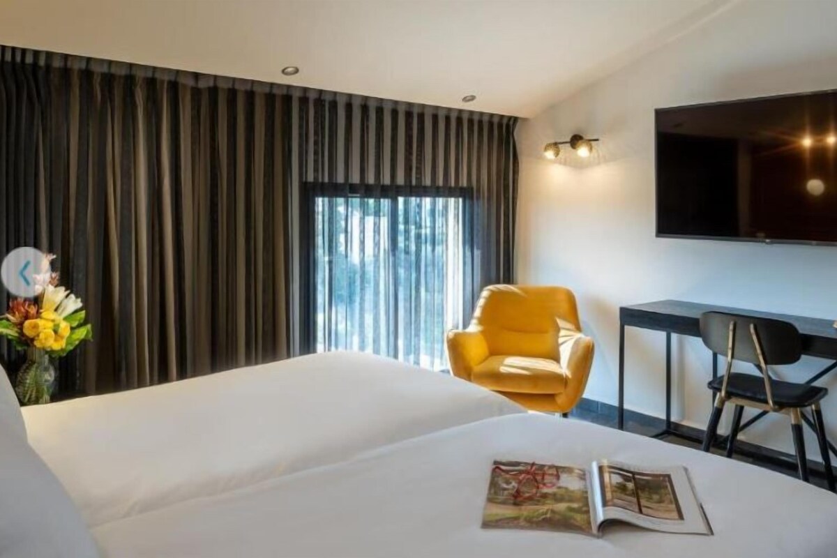 A hotel room with a bed, a desk, a chair, a TV, and a window with curtains.