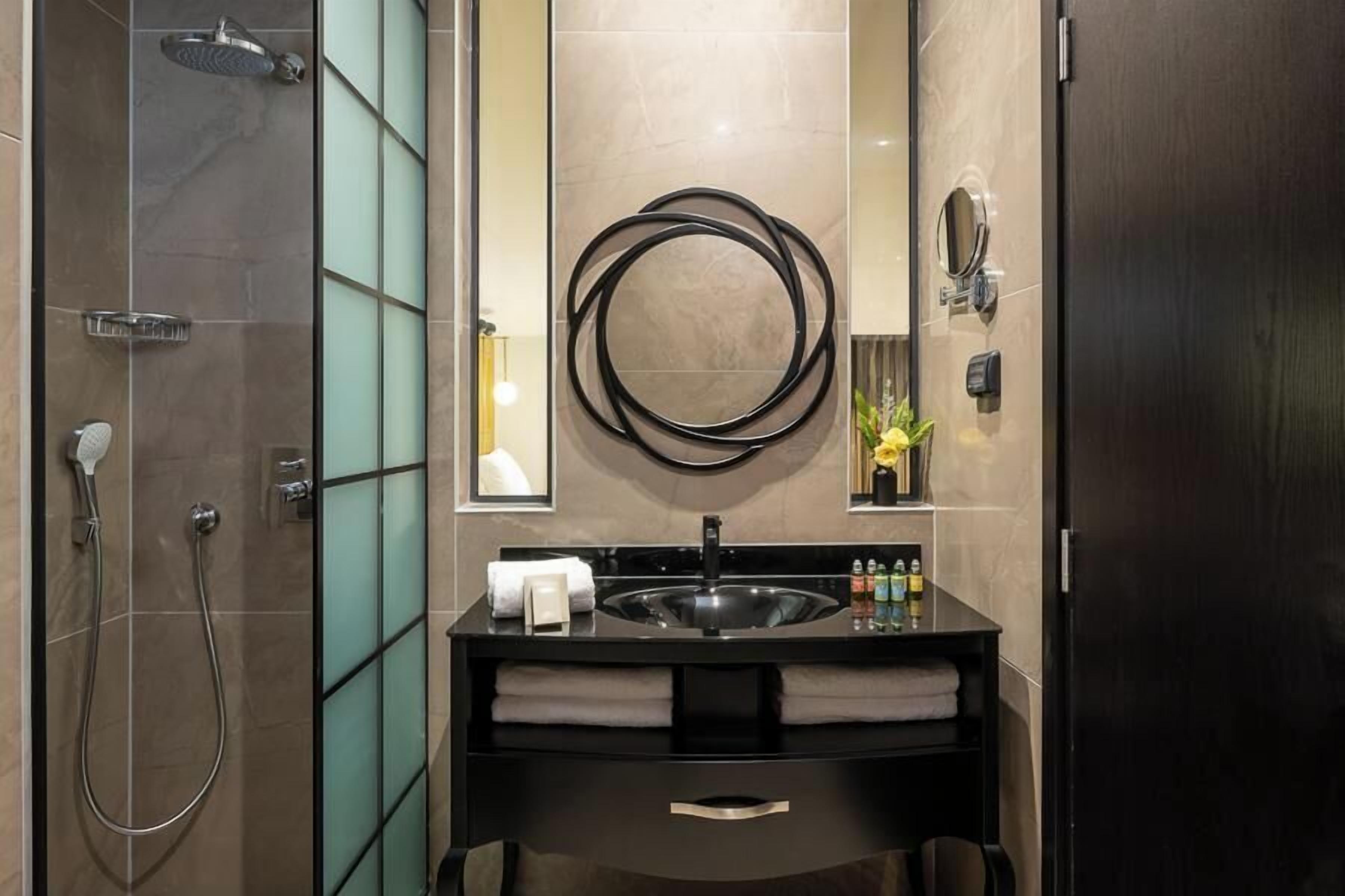 Un baño moderno con cabina de ducha de vidrio, tocador con lavamanos negro y un espejo grande.