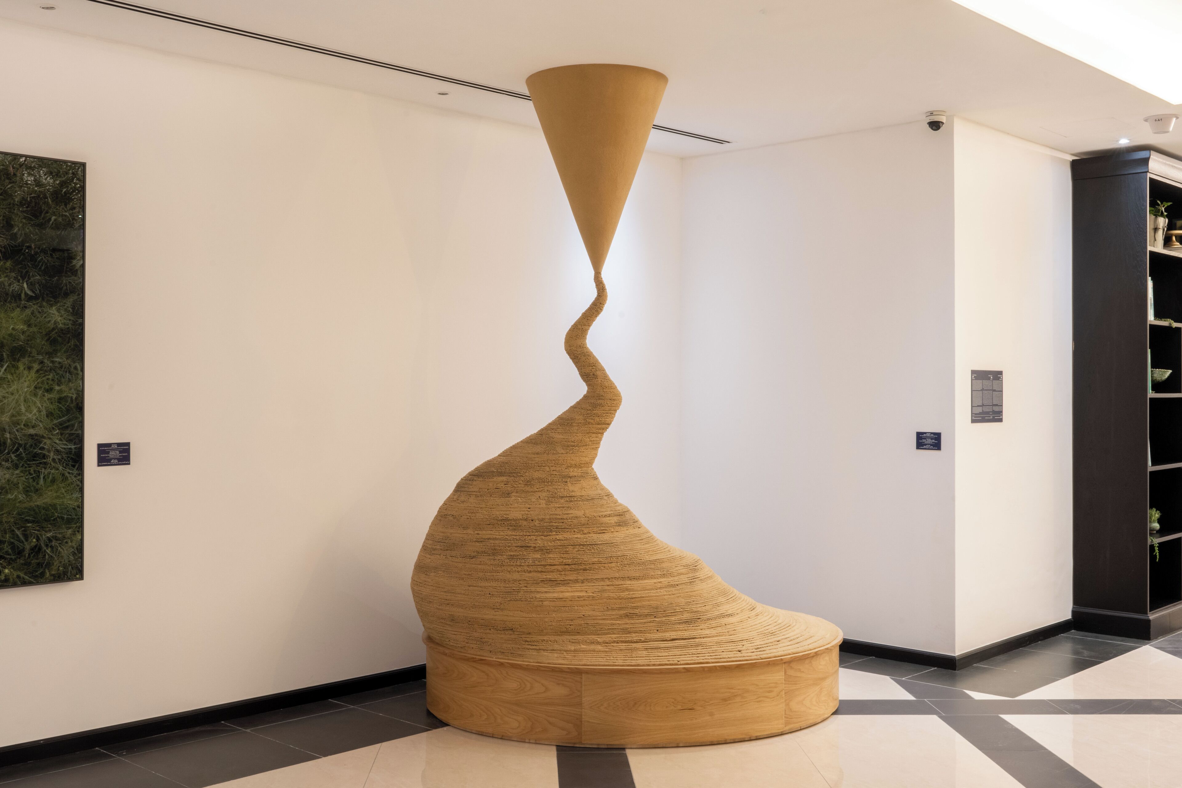 Una instalación de arte moderno en un vestíbulo con diseño espiral, suelo de madera y una gran pintura abstracta en la pared.