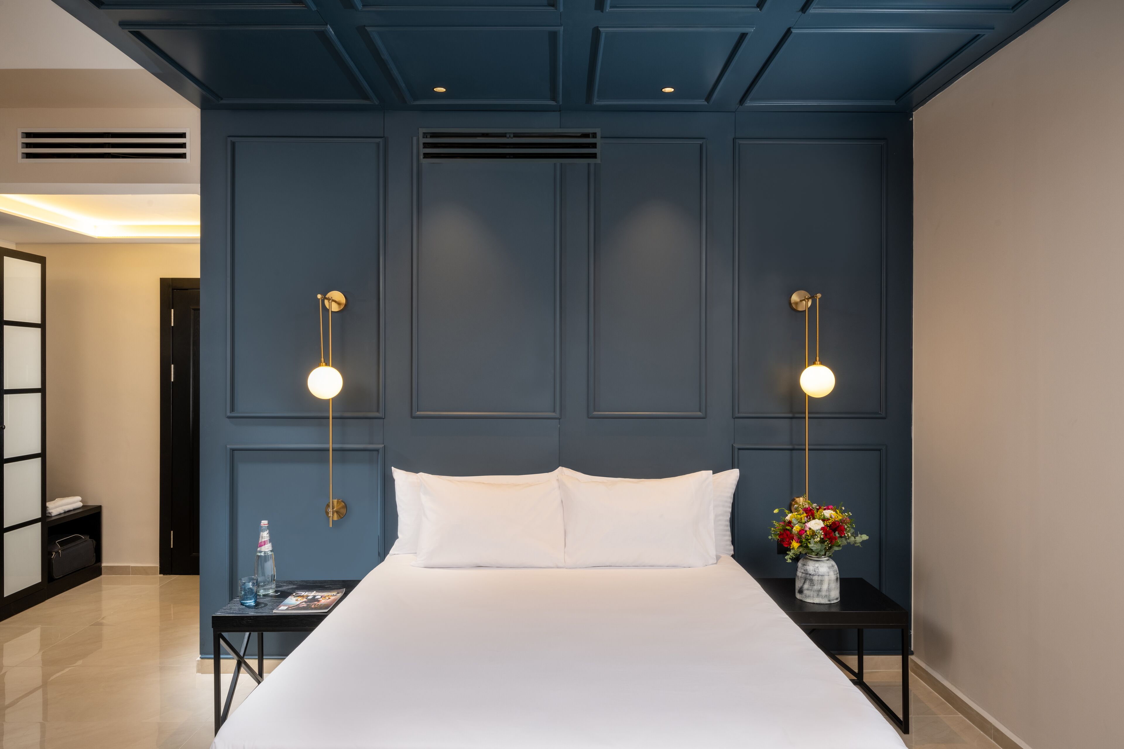 Una habitación de hotel con una cama grande, dos mesitas de noche, un enchufe en la pared y dos apliques de luz.