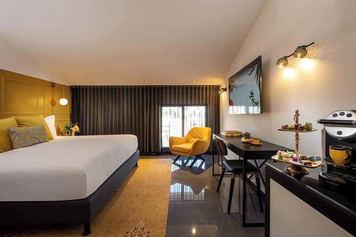 Una habitación de hotel moderna con una cama grande, un escritorio con silla, una mesa de comedor con bufé y un amplio ventanal con cortinas.