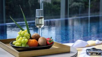 A tray with fruits and a glass of white wine by a poolside with a camera on the table.
