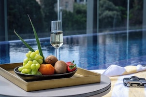 Una bandeja con frutas y una copa de vino blanco junto a una piscina, con una cámara sobre la mesa.