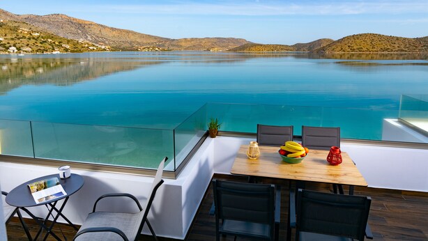 Un'area pranzo esterna moderna con vista su un lago tranquillo e delle colline.