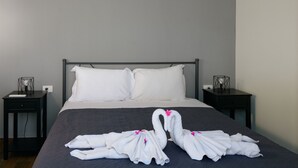 Un letto rifatto con cuscini bianchi e copripiumino scuro, affiancato da due comodini con soprammobili.
